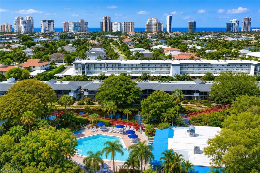 Expansive community featuring a large swimming pool with surrounding lounge chairs and blue umbrellas, surrounded by lush tropical landscaping