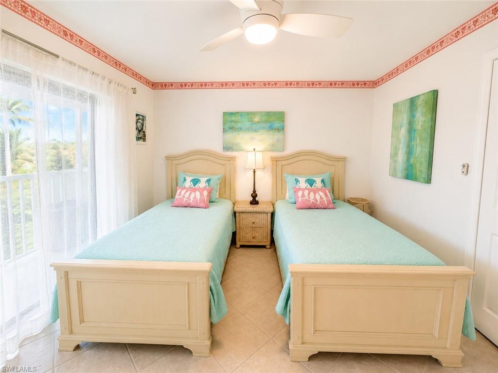 Bedroom featuring two bed frames, a window with sheer curtains, ceiling fan with integrated lighting, and tile flooring
