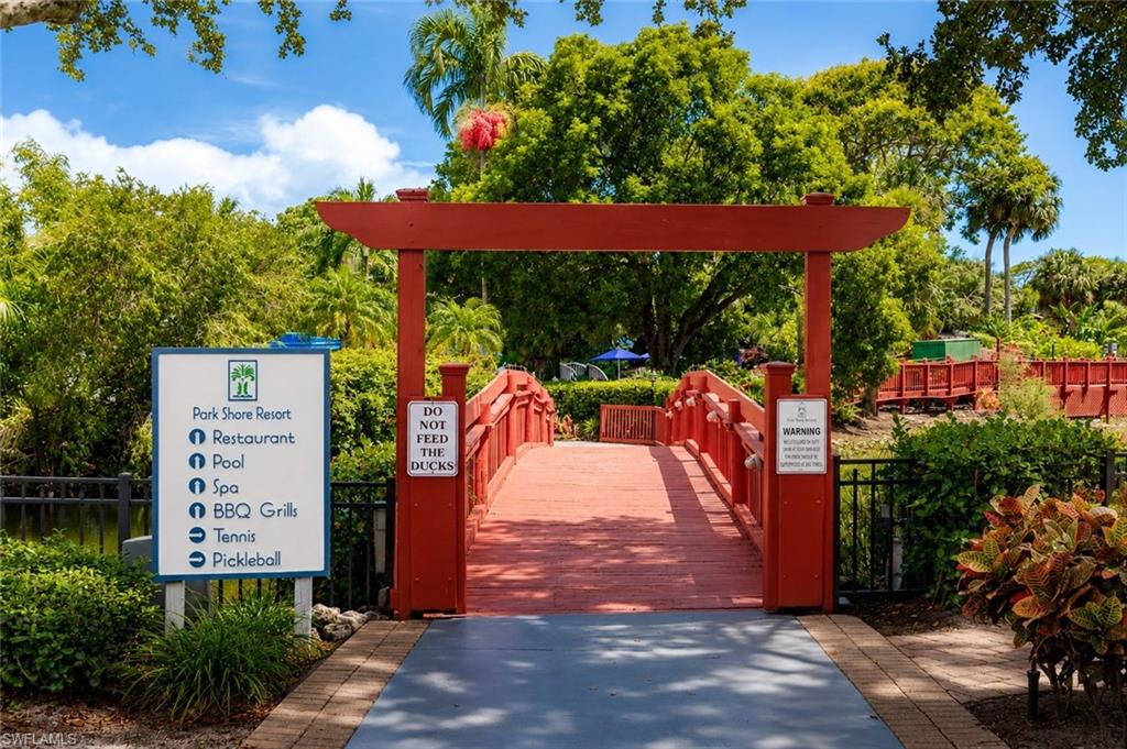 Decorative red wooden archway leading to a bridge, surrounded by lush green foliage and tropical landscaping