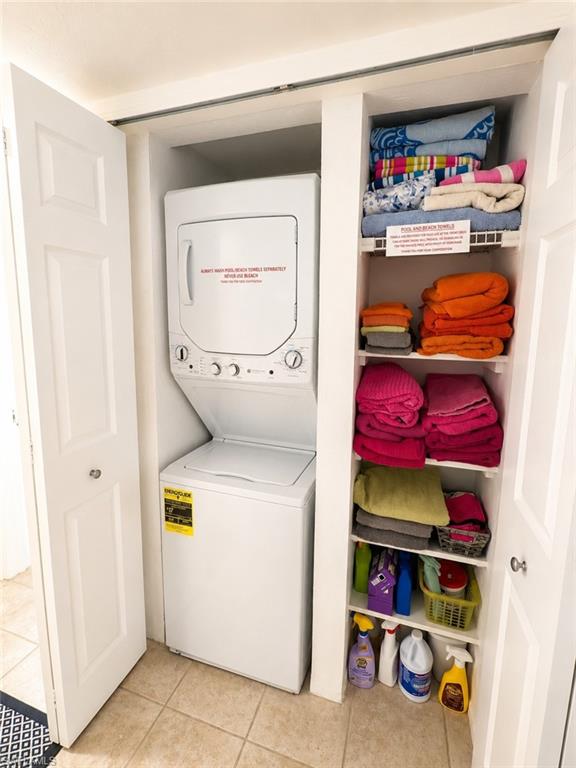 Compact laundry closet featuring a white stacked washer and dryer unit, integrated shelving, and light-toned tile flooring