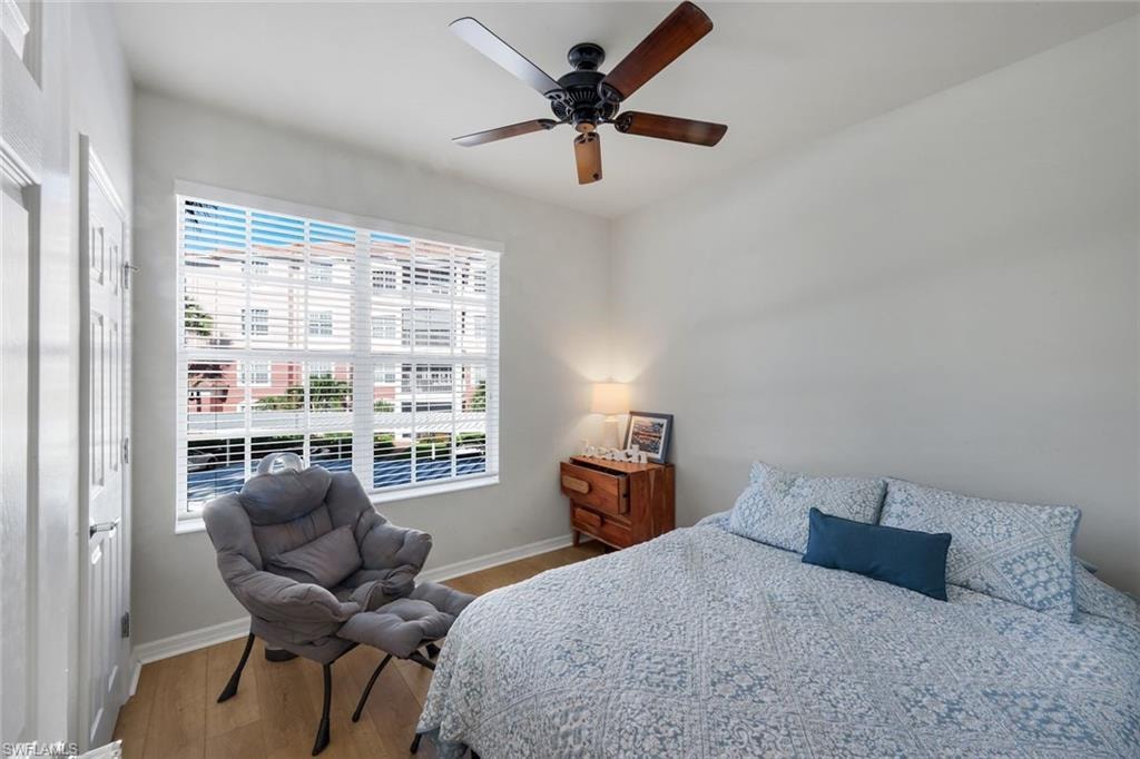 Spacious room featuring wood-finish flooring, a ceiling fan with integrated lighting, and a large window with horizontal blinds