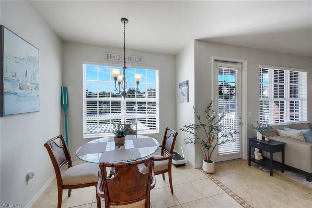 Dining area featuring a large window with horizontal blinds, a glass-top table, and a multi-bulb chandelier