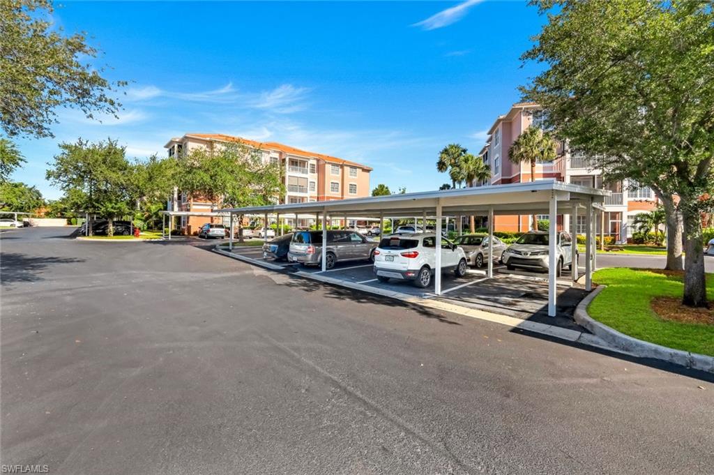 Paved parking area with covered carports, landscaping, and multi-story residential buildings