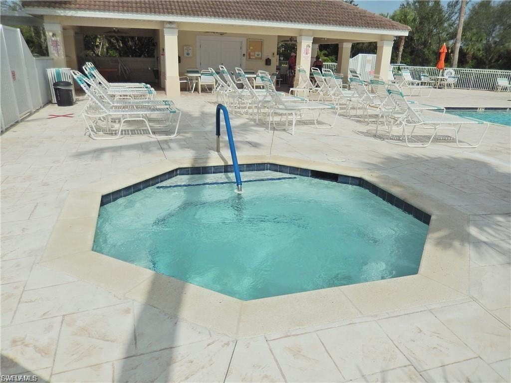 Octagonal hot tub featuring a blue handrail, surrounded by light-toned paver decking