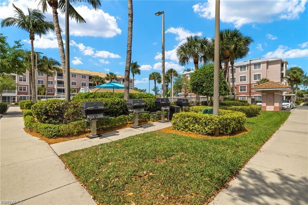 Outdoor grilling station featuring multiple built-in grills, bordered by manicured shrubbery and green lawn