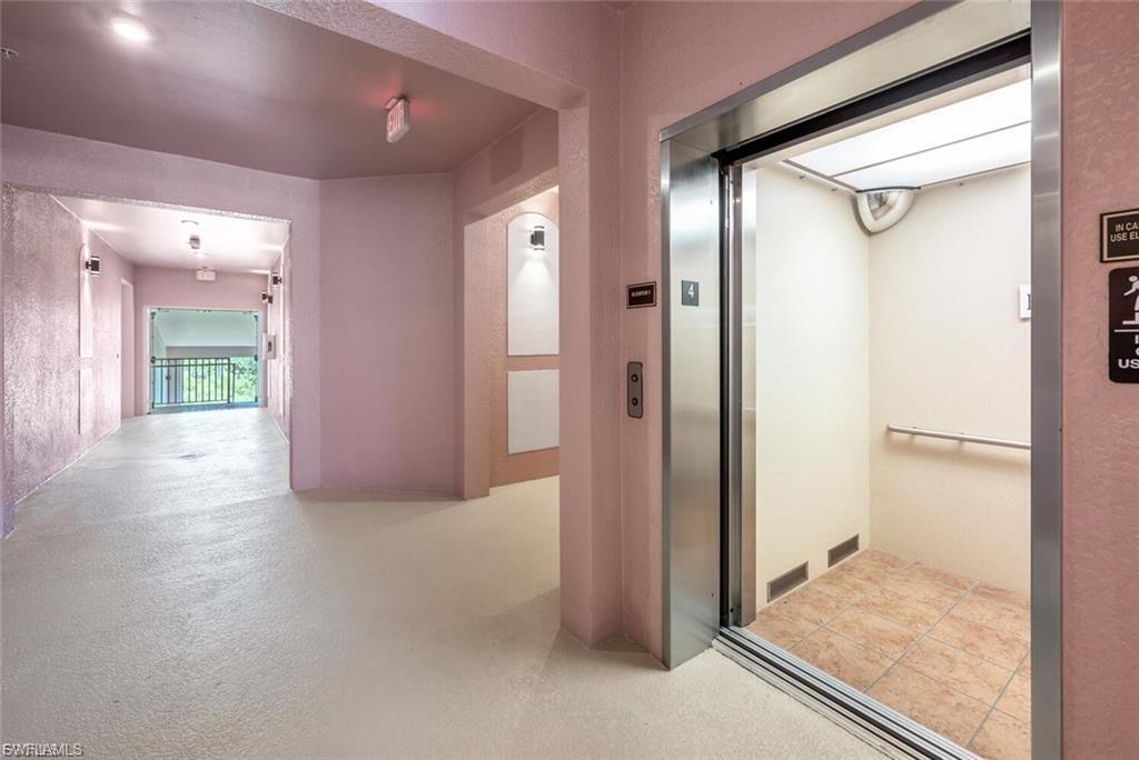Stainless steel elevator with tiled flooring and handrail, situated within a hallway featuring textured walls and recessed lighting