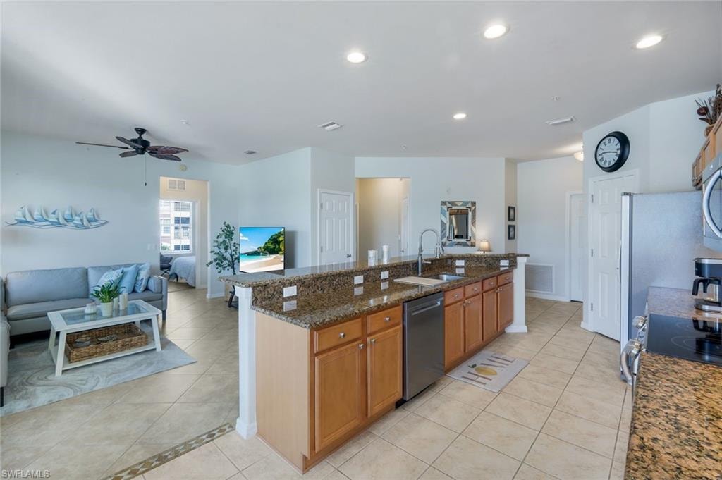 Open-concept living space featuring a kitchen island with granite countertops, wood cabinetry, and stainless steel appliances