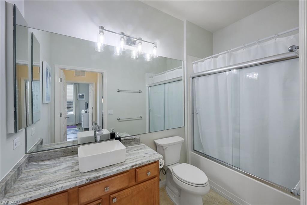 Bathroom featuring a wood-finish vanity with a vessel sink, a stone-finish countertop, and an expansive wall mirror