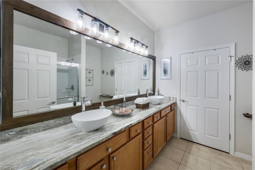 Dual vessel sinks atop a stone-finish countertop with light wood-finish cabinetry