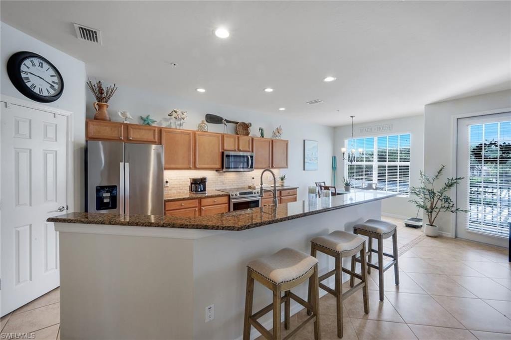 Open-concept kitchen featuring an expansive breakfast bar, recessed lighting, tile flooring, stainless steel appliances, and wood cabinetry