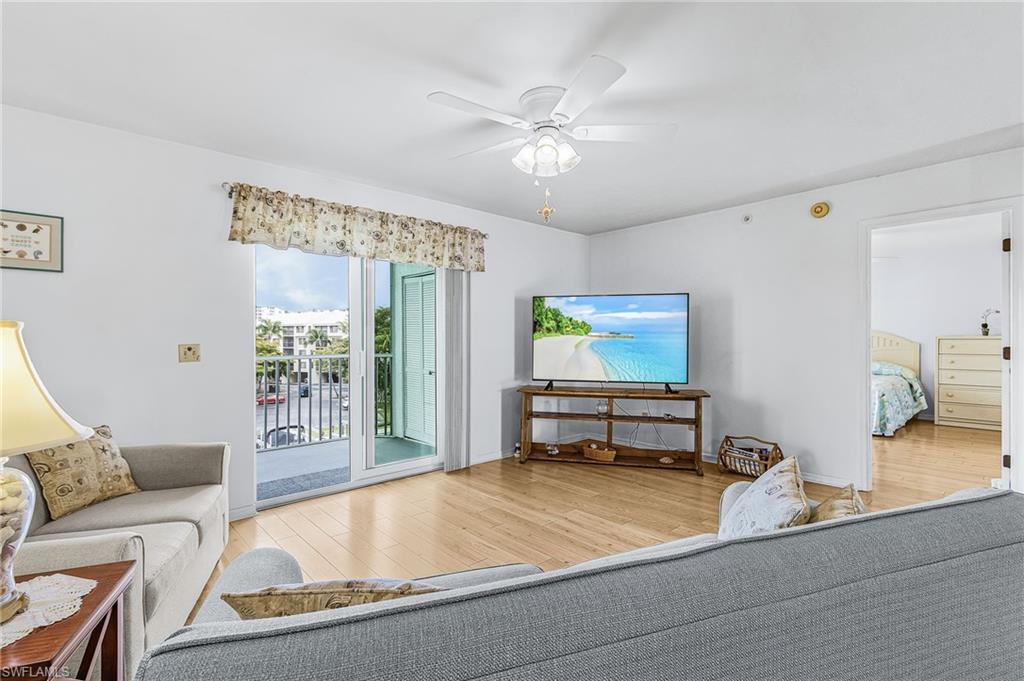 Living area featuring wood-finish flooring, white walls, and a white ceiling fan with integrated lighting