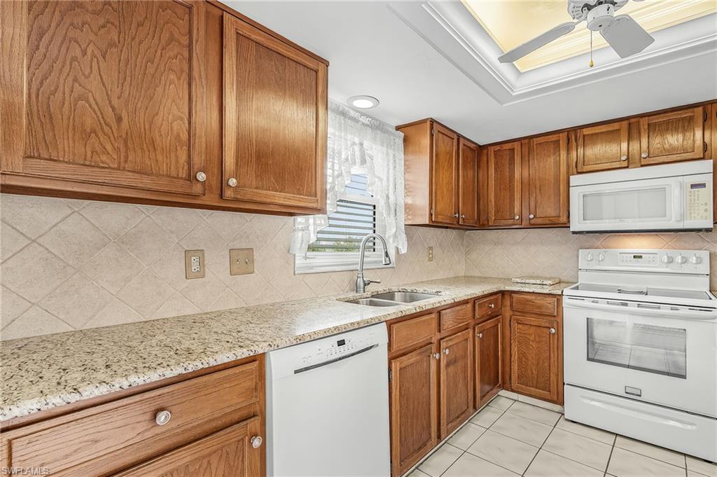 Kitchen featuring warm wood cabinetry, light-toned countertops, a tile backsplash, and matching white appliances