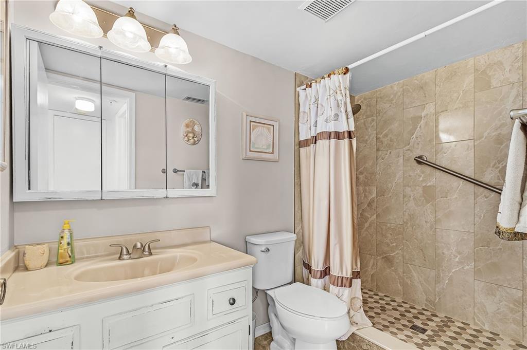 Bathroom featuring a vanity with an integrated sink and base cabinetry, a three-panel mirrored medicine cabinet, a three-light fixture, a toilet, and a tiled shower with a grab bar