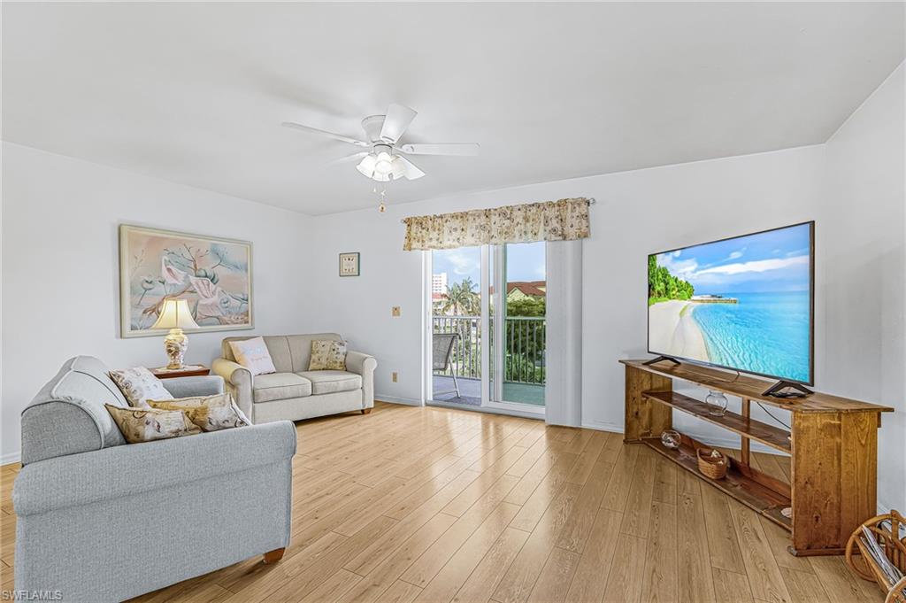 Bright living area featuring wood-finish flooring, a ceiling fan with integrated lighting, and a sliding glass door leading to an outdoor balcony