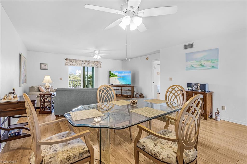 Open-concept dining and living area featuring wood-finish flooring, a ceiling fan, and white walls