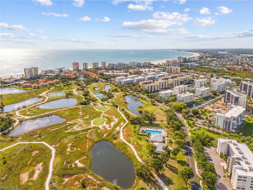 Expansive coastal landscape featuring a broad sandy beach, numerous high-rise buildings, multiple golf course fairways, several water features, and a community swimming pool