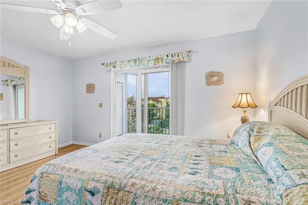 Bedroom featuring sliding glass doors opening to a balcony, wood-finish flooring, a ceiling fan with integrated lighting, and white painted walls