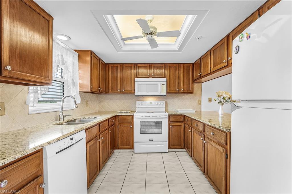 U-shaped kitchen featuring wood cabinetry, granite countertops, white appliances, and a skylight with a ceiling fan