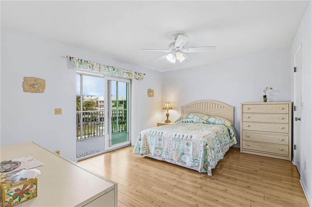 Sliding glass doors opening to an exterior balcony, wood-finish flooring, white walls, and a ceiling fan with integrated lighting