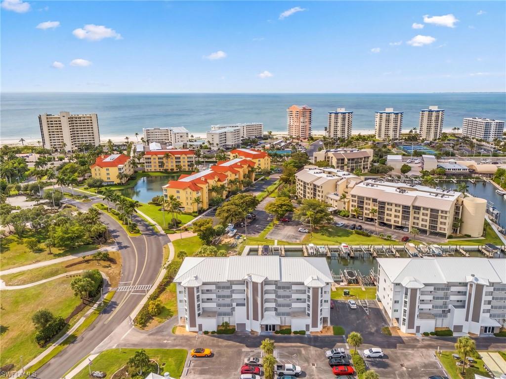 Coastal community with multi-story buildings, marina access, and proximity to a sandy beach and open water