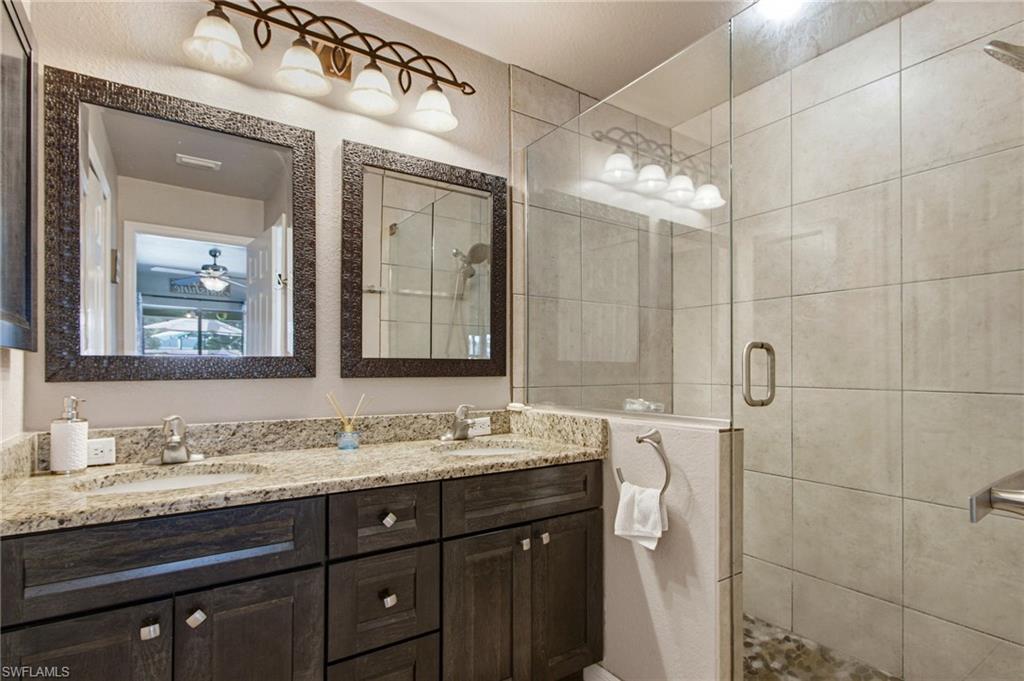 Bathroom featuring a double vanity with stone countertops, a full-width mirror, and a glass-enclosed shower with tiled walls and a natural stone floor