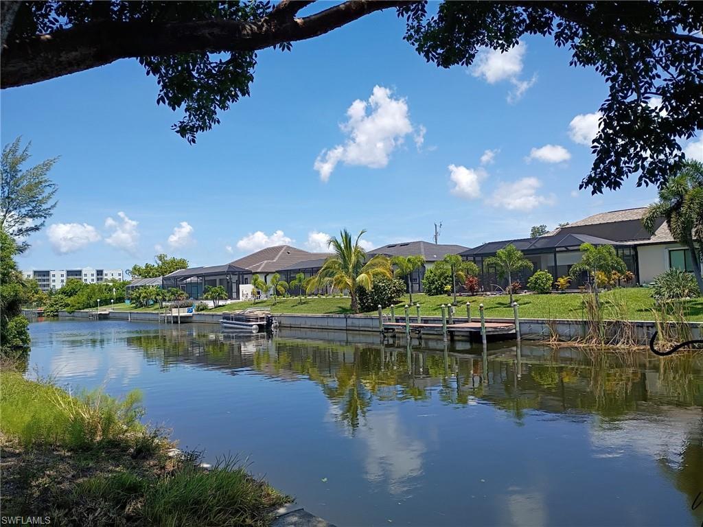 Waterfront property featuring a private boat dock, screened lanai, manicured lawn, and mature tropical landscaping