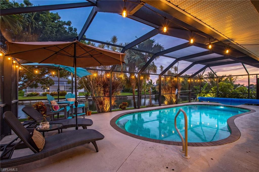 Screened lanai featuring a freeform pool with a curved entry rail, string lighting, and tropical landscaping