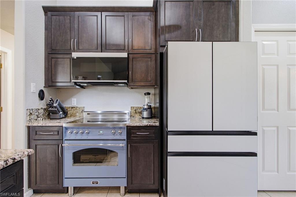 Gourmet kitchen featuring dark wood cabinetry, granite countertops, a built-in microwave, and a professional-grade range with a custom hood
