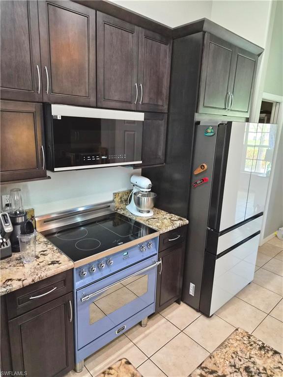 Kitchen showcasing dark wood-finish cabinetry, granite countertops, a built-in microwave, a vibrant blue range with an electric cooktop, and tile flooring