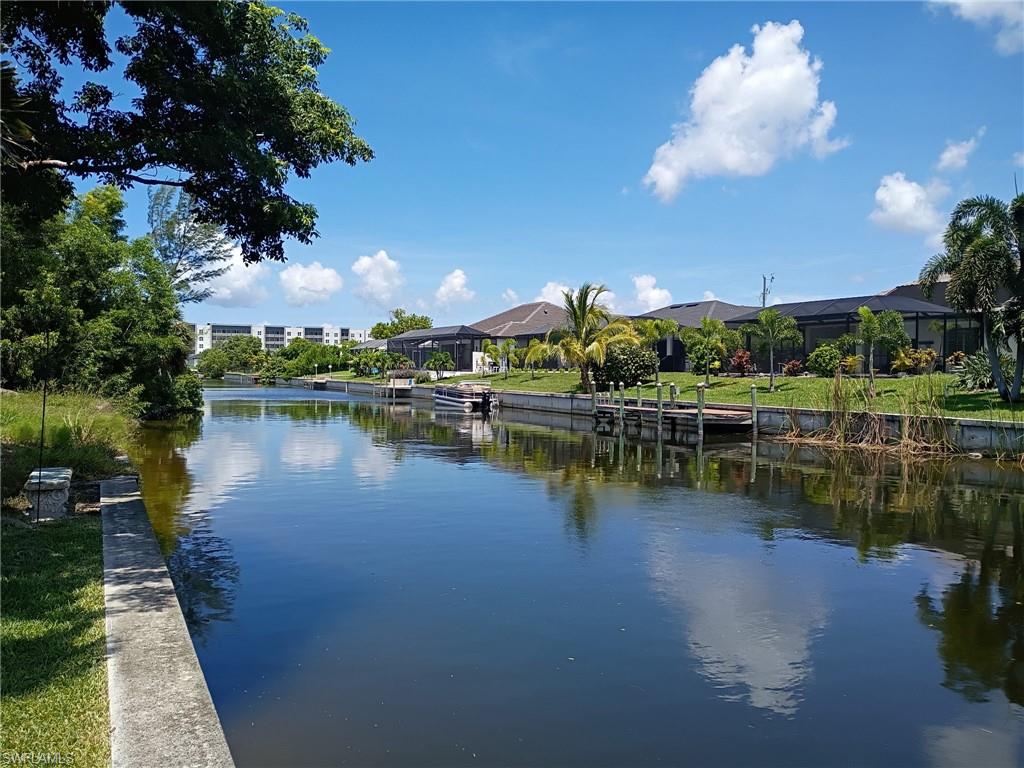 Waterfront property featuring a private boat dock, manicured green lawn, and mature palm trees