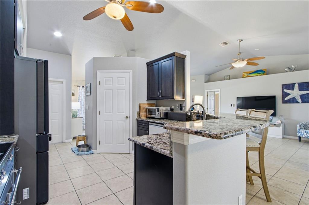 Open-concept kitchen featuring granite countertops, dark wood cabinetry, tile flooring, and vaulted ceilings