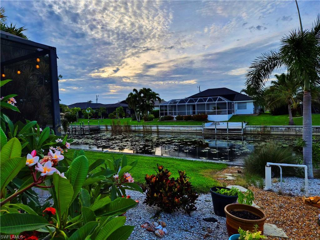 Canal-front property featuring a screened-in patio, mature landscaping, and an adjacent dock