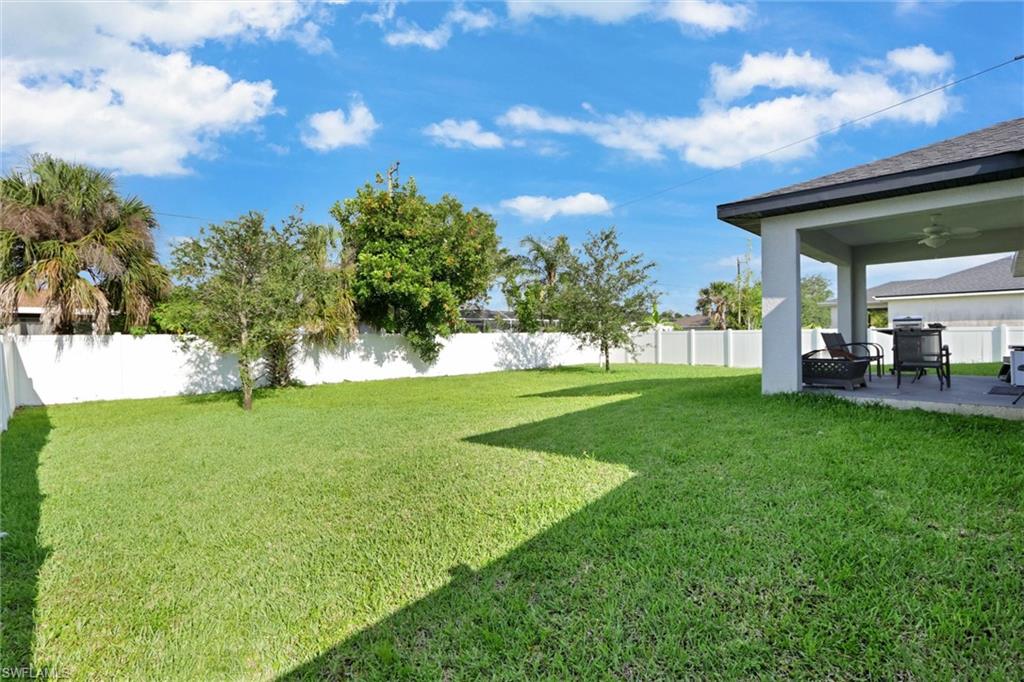 Expansive backyard featuring a lush lawn, white privacy fencing, and mature tropical landscaping