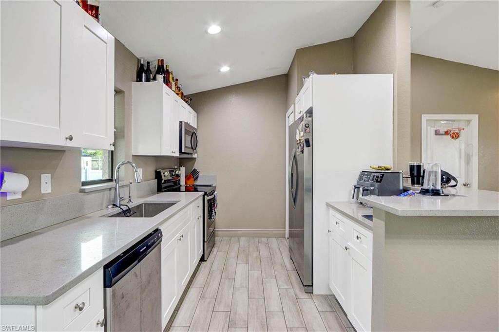 Kitchen featuring white cabinetry, light-toned countertops, wood-finish flooring, stainless steel appliances, and vaulted ceilings