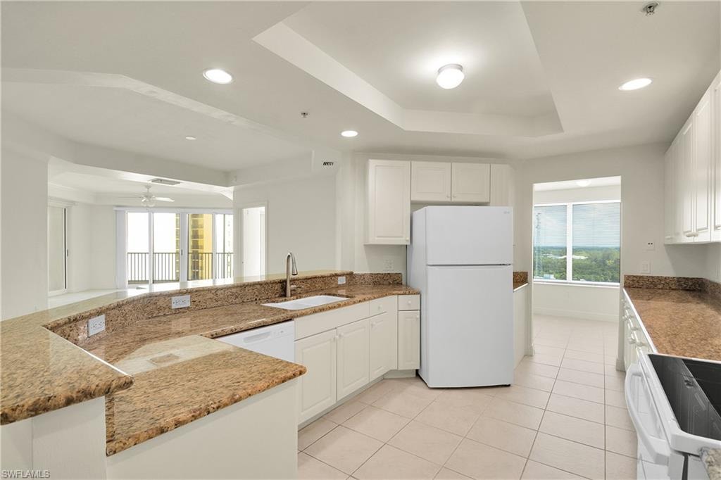 Kitchen featuring a raised ceiling, white cabinets, white appliances, a peninsula, and light tile patterned floors