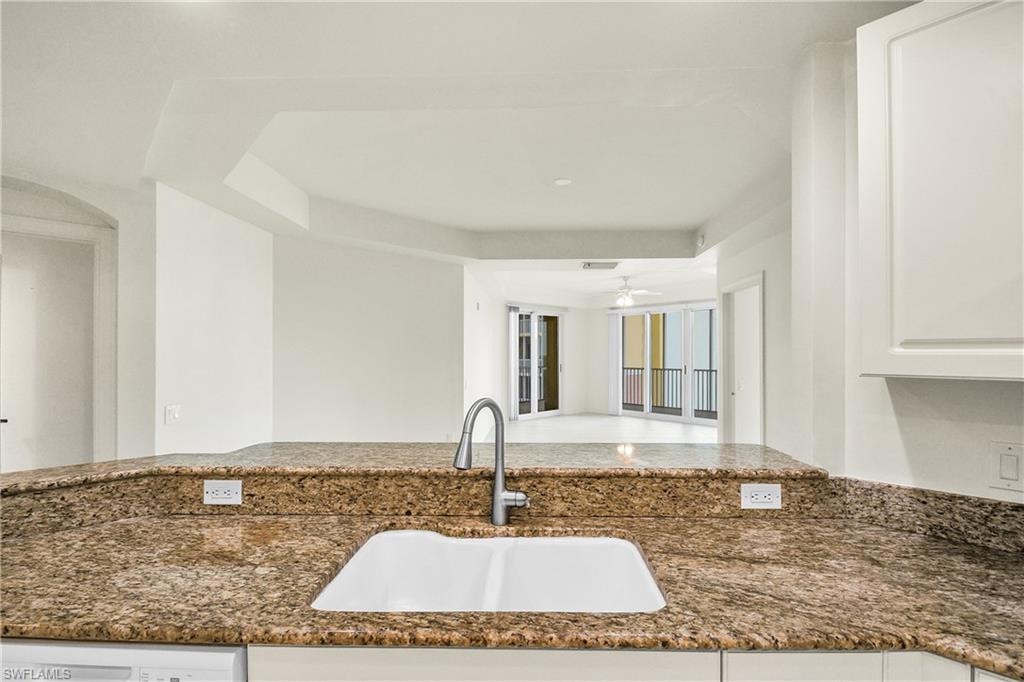 Kitchen with white cabinets, dark stone counters, open floor plan, and ceiling fan