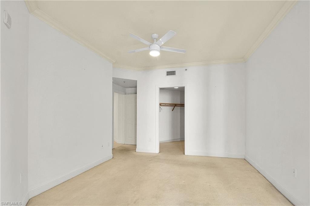 Unfurnished bedroom featuring a ceiling fan, crown molding, a walk in closet, and light colored carpet