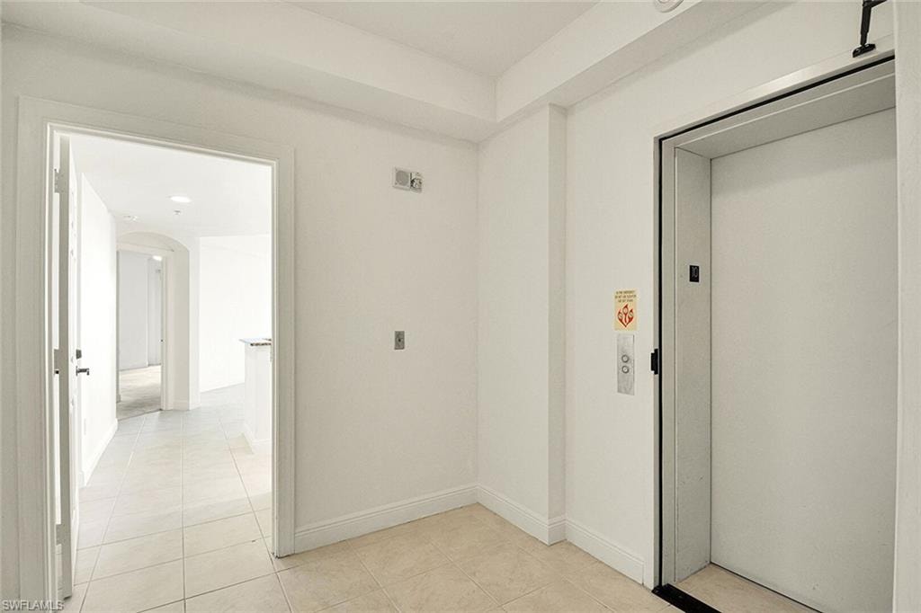 Hall featuring elevator, light tile patterned floors, and arched walkways