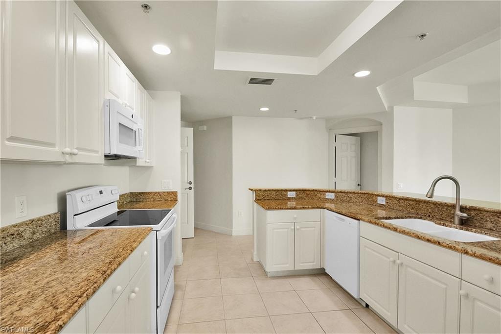 Kitchen featuring white appliances, recessed lighting, a tray ceiling, white cabinets, and light stone counters