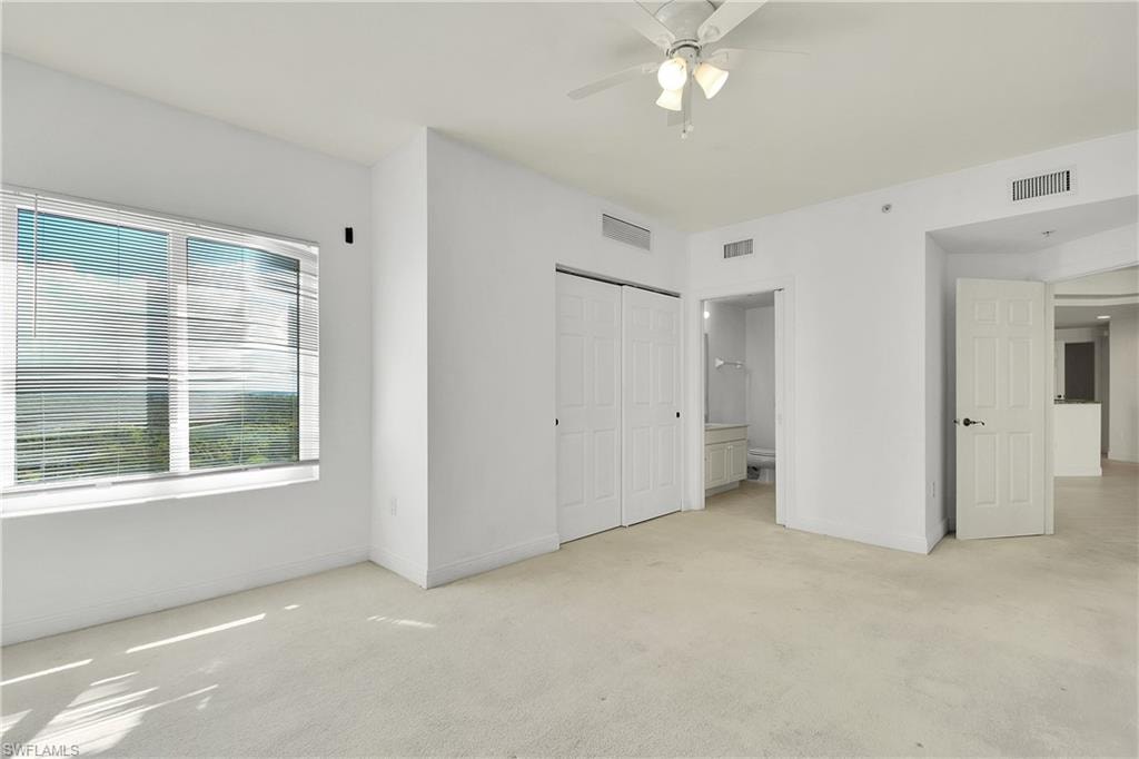 Unfurnished bedroom with light carpet, a closet, ceiling fan, and ensuite bath