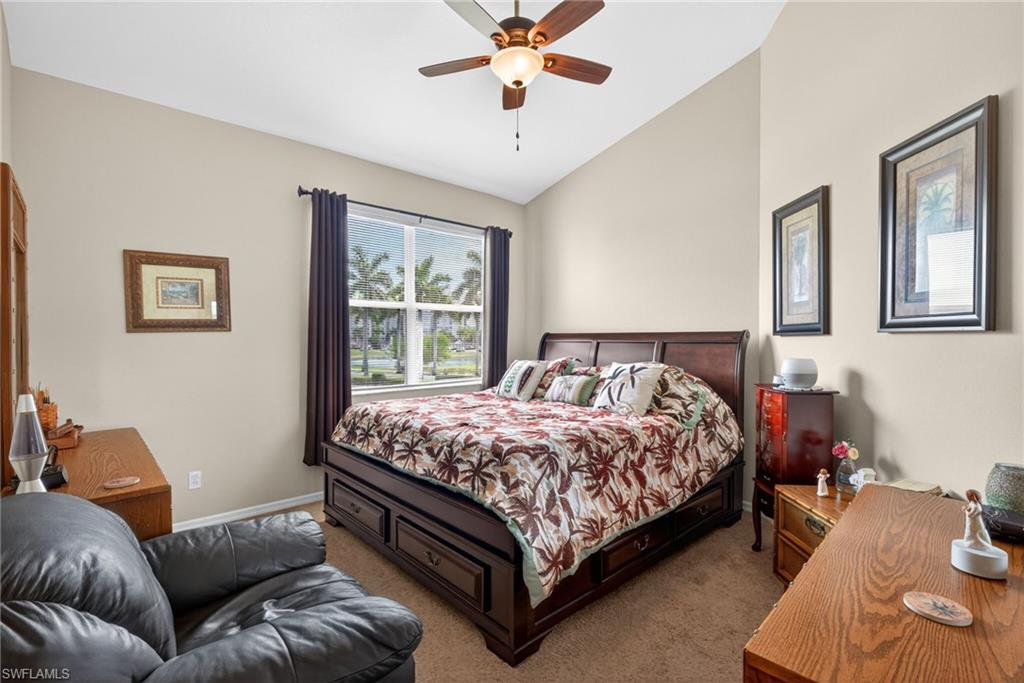Spacious bedroom featuring vaulted ceilings, a ceiling fan with integrated lighting, and a large window with exterior landscaping views