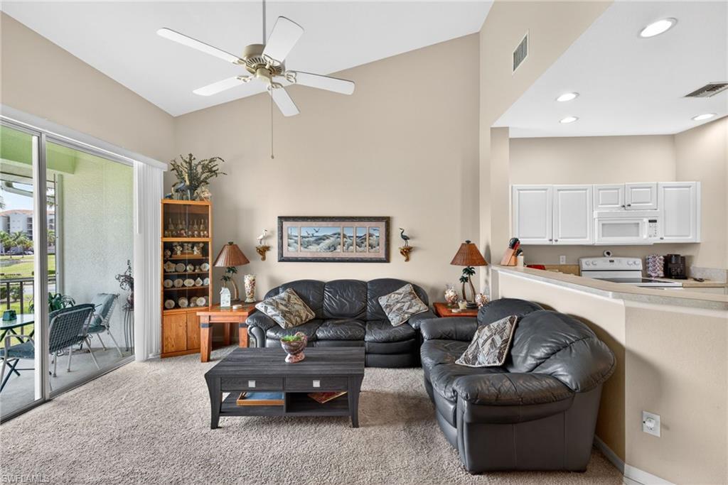 Living area featuring vaulted ceilings, a ceiling fan, plush carpet flooring, and sliding glass door access to a private balcony