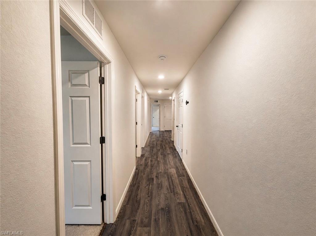 Long corridor featuring wood-finish flooring, white walls, recessed lighting, and multiple paneled doors with black hardware