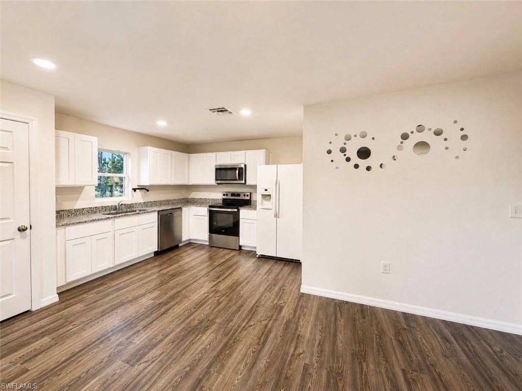 Open-concept kitchen featuring white cabinetry, granite countertops, stainless steel appliances, wood-finish flooring, and recessed lighting