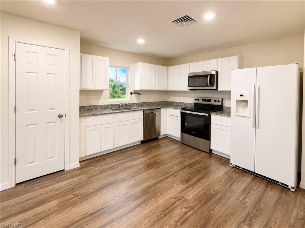 Kitchen featuring wood-finish flooring, white cabinetry, speckled countertops, and stainless steel appliances including a range, microwave, and dishwasher