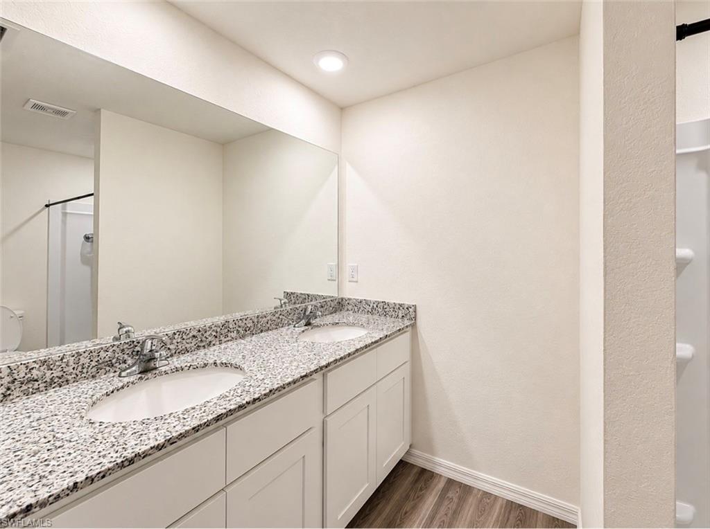 Dual vanity featuring light-toned cabinetry and speckled countertops