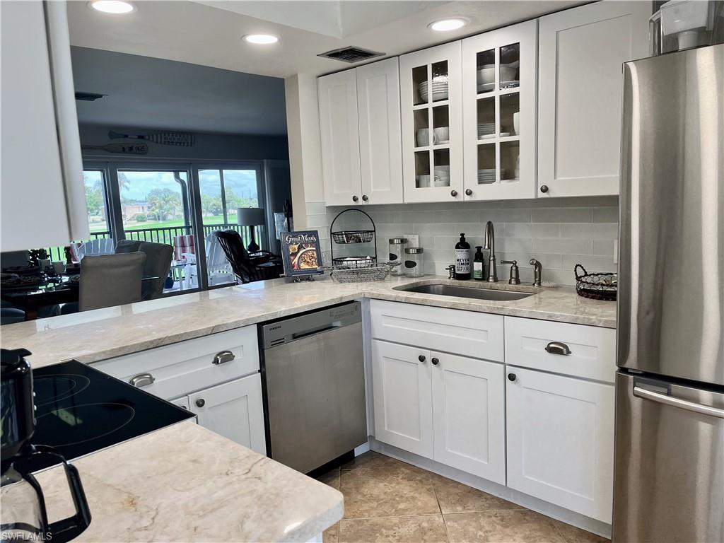 Updated Kitchen with stainless steel appliances, recessed lighting, glass insert cabinets, white cabinets, and tile flooring
