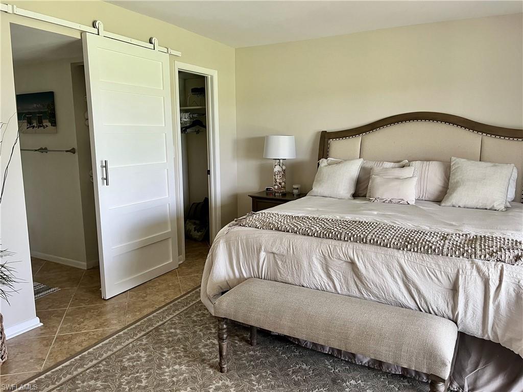 Tiled primary bedroom featuring a king bed with a barn door to bathroom and a spacious closet