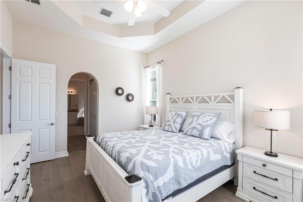Bedroom featuring a tray ceiling with a ceiling fan, wood-finish flooring, and an arched doorway