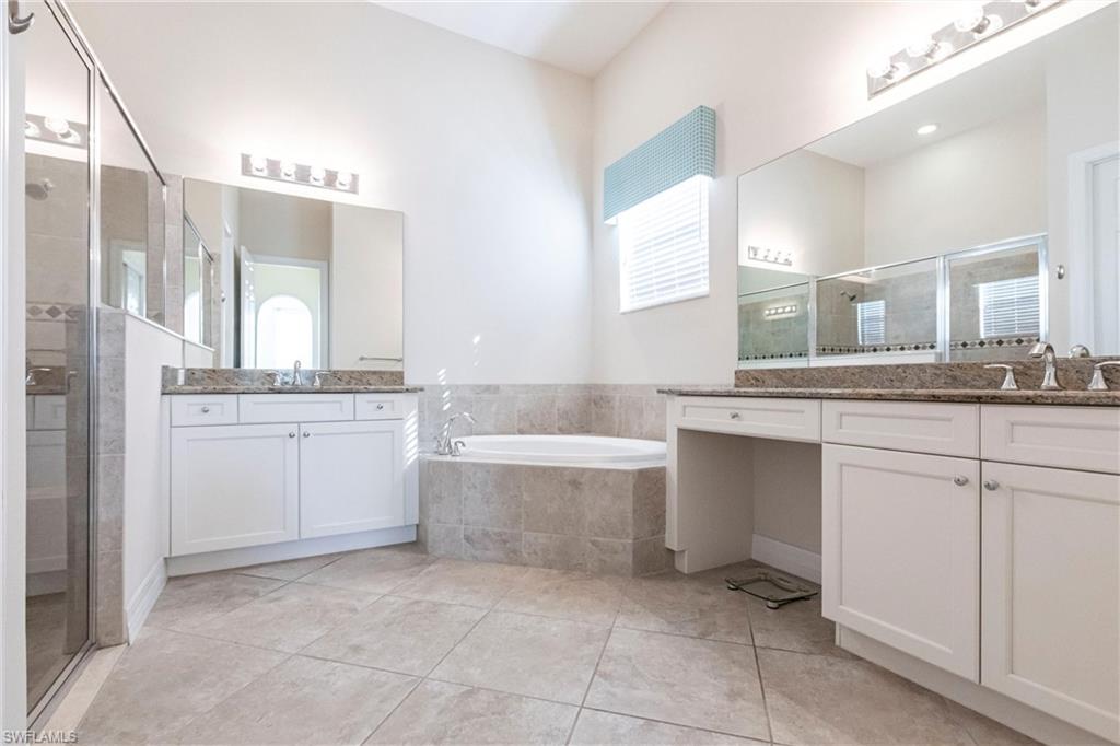 Spacious bathroom featuring a built-in soaking tub, dual vanity with granite countertops, tile flooring, and a glass-enclosed shower